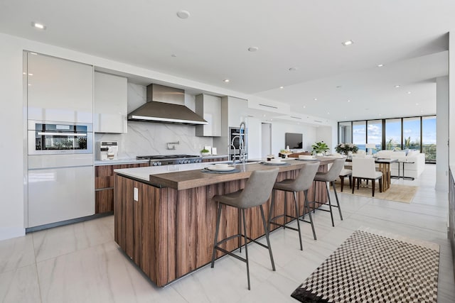 kitchen with sink, oven, a kitchen island with sink, wall chimney range hood, and backsplash