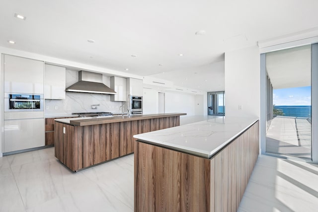 kitchen with white cabinets, wall chimney range hood, oven, and decorative backsplash