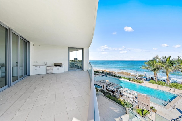 balcony featuring a beach view, a water view, and exterior kitchen