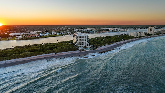 aerial view at dusk featuring a water view and a beach view