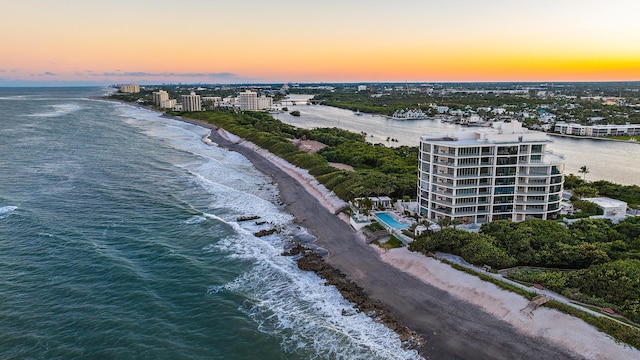 aerial view at dusk featuring a water view and a beach view