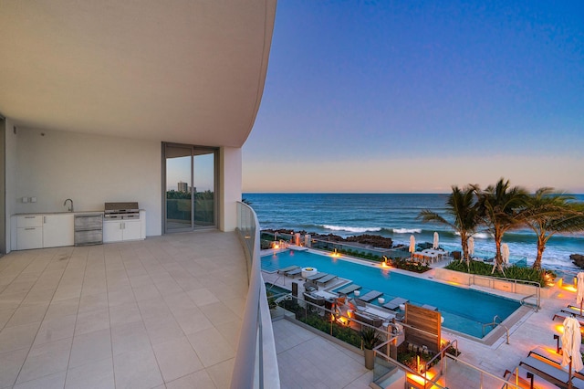 pool at dusk with exterior kitchen and a water view