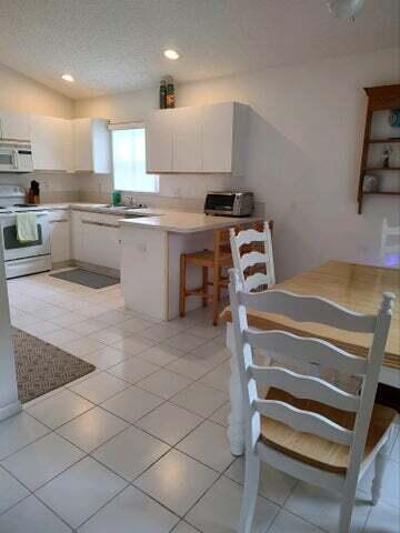 kitchen with a textured ceiling, light tile patterned flooring, white appliances, and white cabinetry