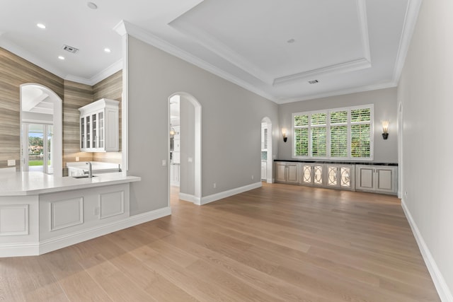 interior space with sink, a raised ceiling, crown molding, and light hardwood / wood-style flooring