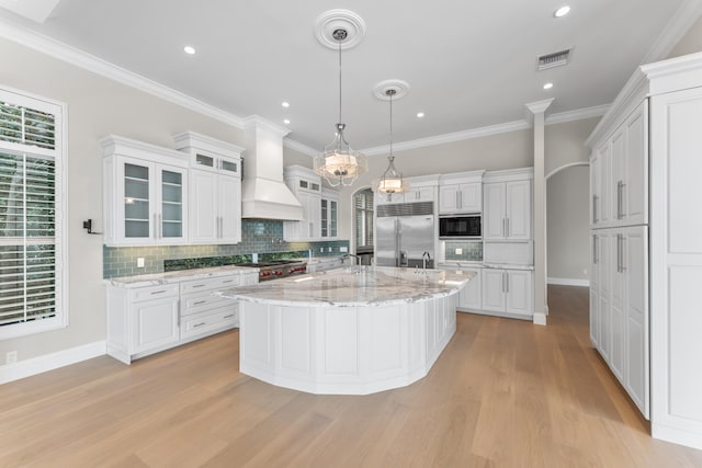 kitchen with premium range hood, white cabinetry, a center island with sink, and built in appliances