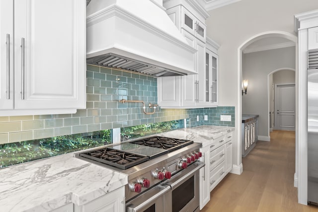 kitchen featuring premium range hood, white cabinetry, range with two ovens, ornamental molding, and light stone counters