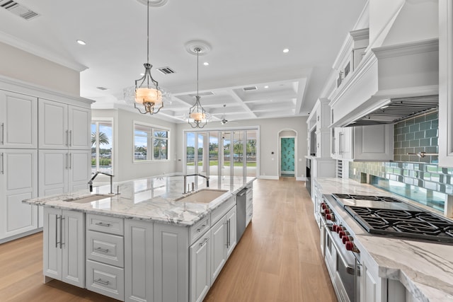 kitchen with pendant lighting, beamed ceiling, sink, coffered ceiling, and a kitchen island with sink