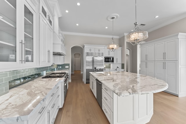 kitchen with a large island with sink, built in appliances, white cabinetry, and pendant lighting