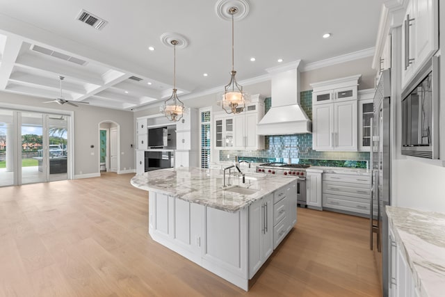 kitchen featuring custom exhaust hood, beamed ceiling, coffered ceiling, an island with sink, and white cabinets