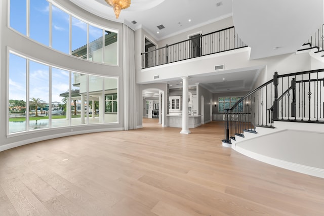 unfurnished living room featuring a high ceiling, light hardwood / wood-style floors, a water view, decorative columns, and crown molding