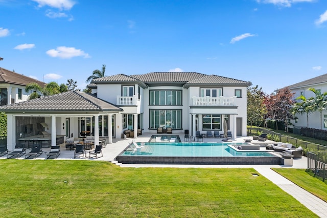 back of house with a balcony, a patio area, a pool with hot tub, and an outdoor kitchen