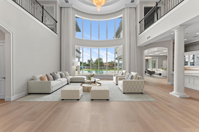 living room featuring light hardwood / wood-style floors, a high ceiling, ornate columns, and a notable chandelier