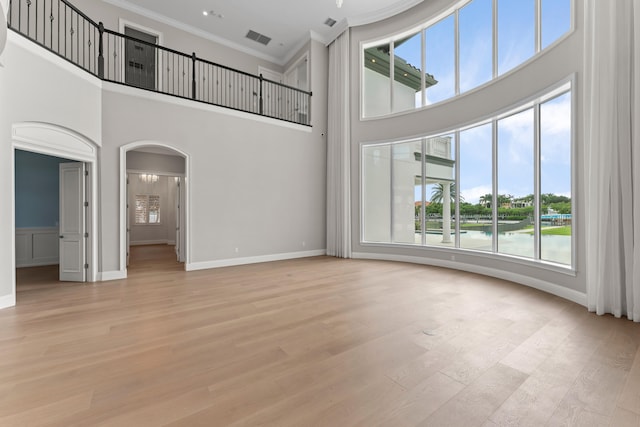 unfurnished living room with a high ceiling, light hardwood / wood-style flooring, crown molding, and a water view