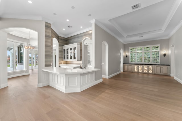 interior space with light wood-type flooring, kitchen peninsula, a notable chandelier, and ornamental molding