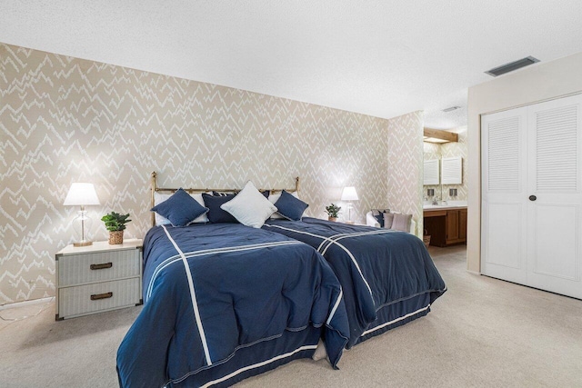 bedroom featuring a closet, ensuite bathroom, and light carpet