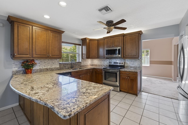 kitchen featuring kitchen peninsula, appliances with stainless steel finishes, light stone counters, ceiling fan, and sink