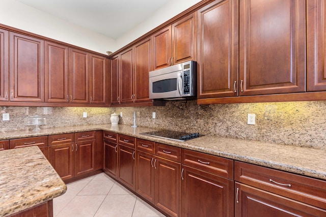kitchen with light stone countertops, black electric cooktop, stainless steel microwave, light tile patterned floors, and backsplash