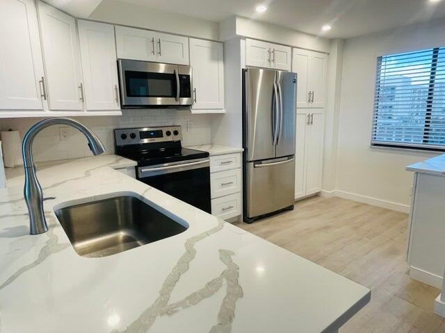 kitchen featuring light stone counters, white cabinets, stainless steel appliances, light wood-type flooring, and sink