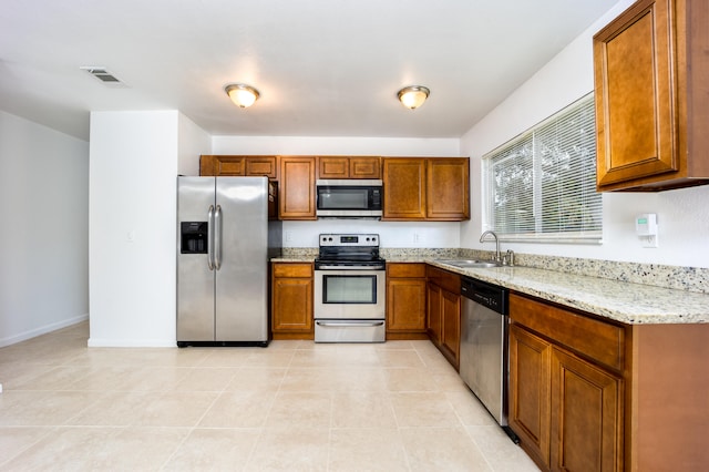 kitchen with appliances with stainless steel finishes, sink, light stone counters, and light tile patterned floors