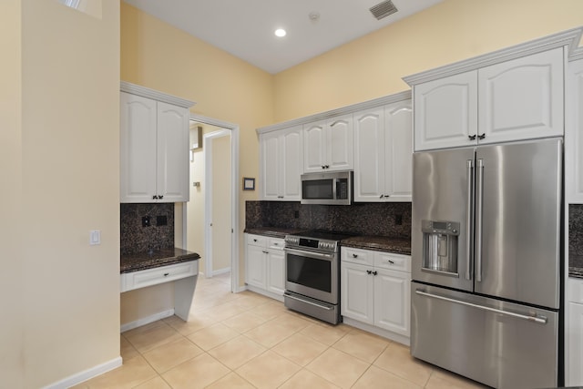 kitchen featuring dark stone countertops, appliances with stainless steel finishes, white cabinetry, and light tile patterned floors