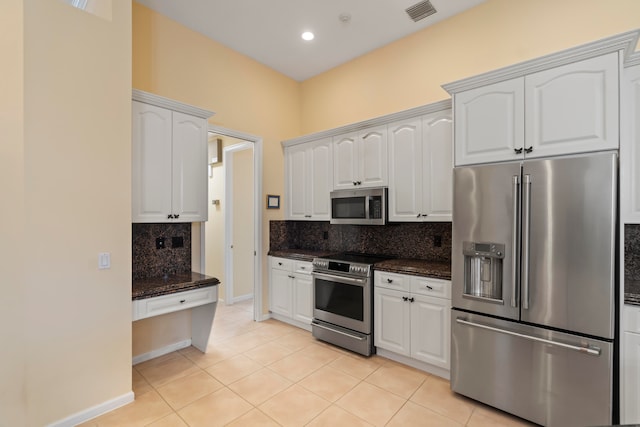 kitchen featuring light tile patterned floors, backsplash, white cabinetry, dark stone countertops, and stainless steel appliances