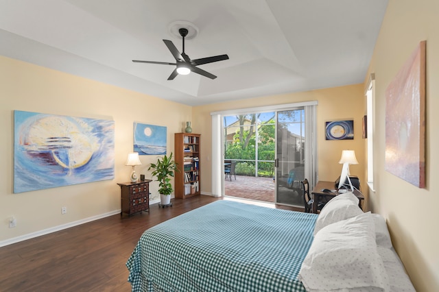 bedroom featuring a tray ceiling, dark hardwood / wood-style floors, access to outside, and ceiling fan