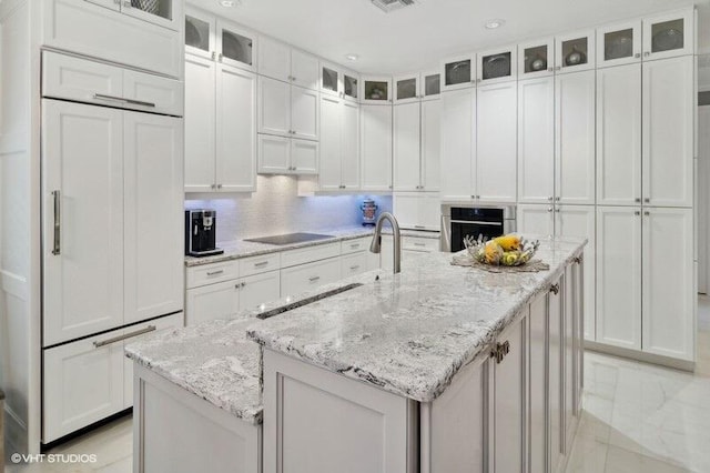 kitchen featuring an island with sink, oven, and white cabinetry