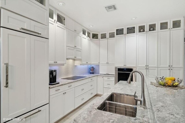 kitchen with white cabinets, sink, tasteful backsplash, oven, and light stone countertops