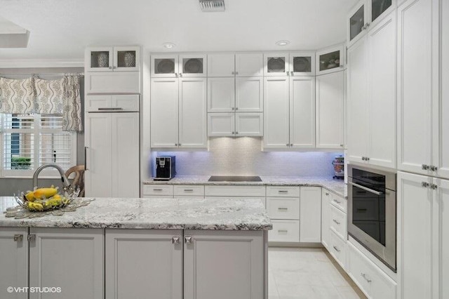 kitchen featuring white cabinetry, decorative backsplash, oven, black electric cooktop, and light stone countertops