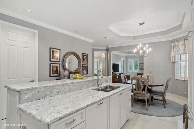 kitchen featuring a kitchen island with sink, sink, white cabinetry, hanging light fixtures, and ornamental molding