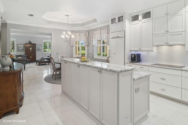 kitchen with decorative backsplash, white cabinets, crown molding, decorative light fixtures, and a center island with sink