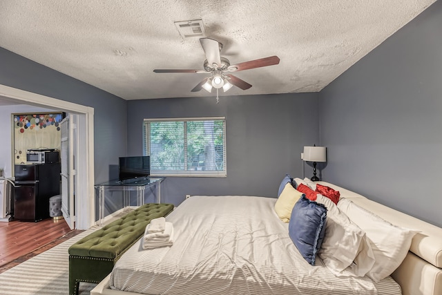 bedroom with hardwood / wood-style flooring, ceiling fan, black fridge, and a textured ceiling