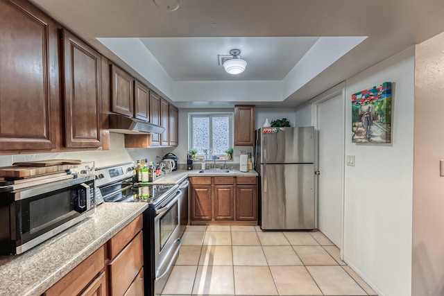 kitchen featuring light stone countertops, sink, stainless steel appliances, a tray ceiling, and light tile patterned flooring