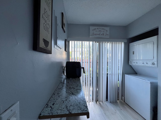 laundry area with stacked washer and clothes dryer, a textured ceiling, and light hardwood / wood-style floors