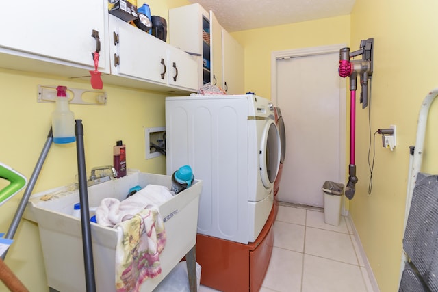 laundry room featuring light tile patterned floors, a textured ceiling, washing machine and dryer, and cabinets