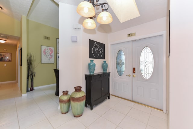 entryway with light tile patterned flooring, an inviting chandelier, and a skylight