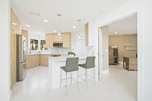 kitchen featuring light brown cabinetry, appliances with stainless steel finishes, kitchen peninsula, hanging light fixtures, and a breakfast bar area