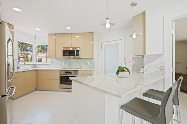 kitchen featuring light brown cabinetry, kitchen peninsula, stainless steel appliances, pendant lighting, and a breakfast bar area