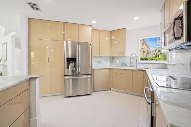 kitchen featuring light brown cabinets, stainless steel appliances, sink, light stone counters, and tasteful backsplash