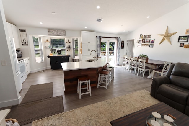 kitchen with white cabinets, dark hardwood / wood-style flooring, lofted ceiling, a center island with sink, and sink