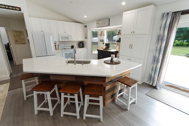 kitchen featuring a large island, a breakfast bar, sink, vaulted ceiling, and white appliances