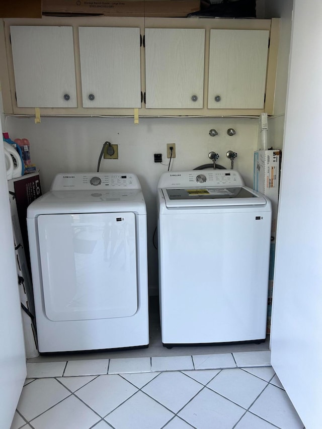 washroom featuring washing machine and dryer, light tile patterned flooring, and cabinets