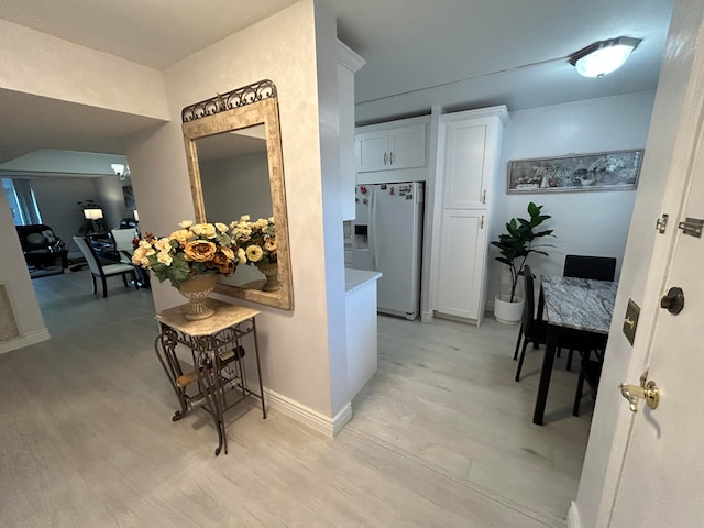 kitchen with white cabinets, white fridge with ice dispenser, and light wood-type flooring