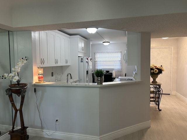 kitchen with light wood-type flooring, kitchen peninsula, white fridge with ice dispenser, and white cabinetry