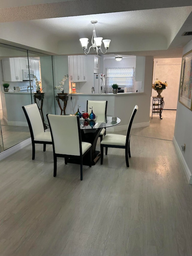 dining space with light wood-type flooring, a textured ceiling, and an inviting chandelier