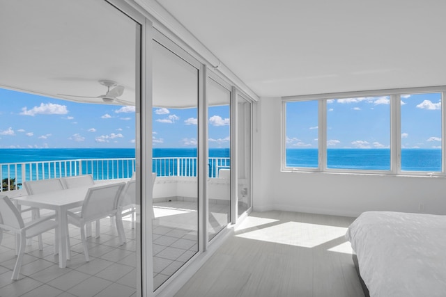 sunroom featuring ceiling fan, a water view, and a view of the beach