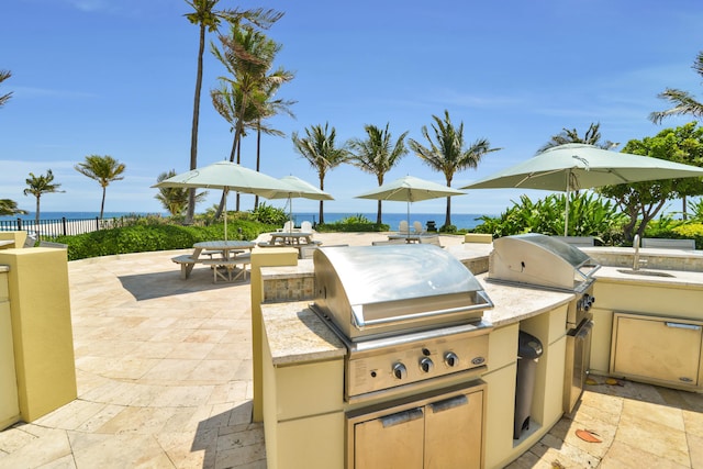 view of patio / terrace featuring an outdoor kitchen, a water view, sink, and grilling area