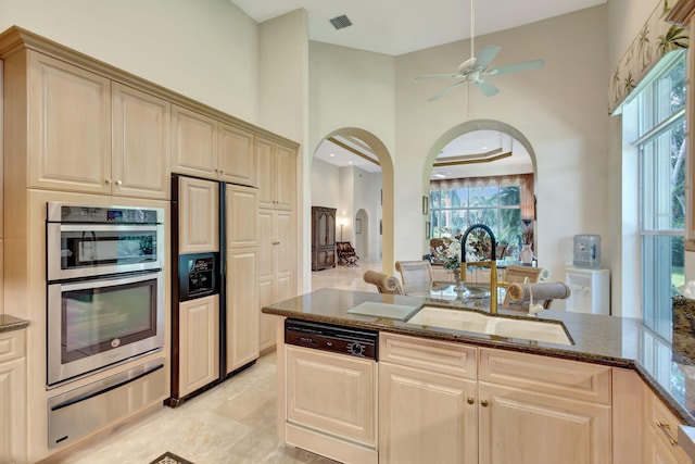 kitchen with arched walkways, a sink, paneled appliances, a warming drawer, and dark stone countertops