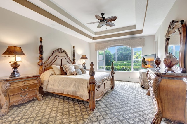 bedroom with light carpet, ceiling fan, and a tray ceiling