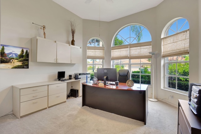 office space with a healthy amount of sunlight, ceiling fan, a towering ceiling, and light colored carpet